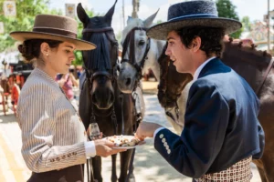 Pareja con trajes típicos comiendo y bebiendo en la Feria del Caballo. Esta imagen se utiliza para ilustrar una entrada sobre la Feria del Caballo de Jerez.