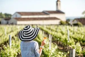 Mujer de espaldas con una copa de vino frente a un viñedo. Esta imagen se utiliza para ilustrar una entrada sobre los beneficios del enoturismo.