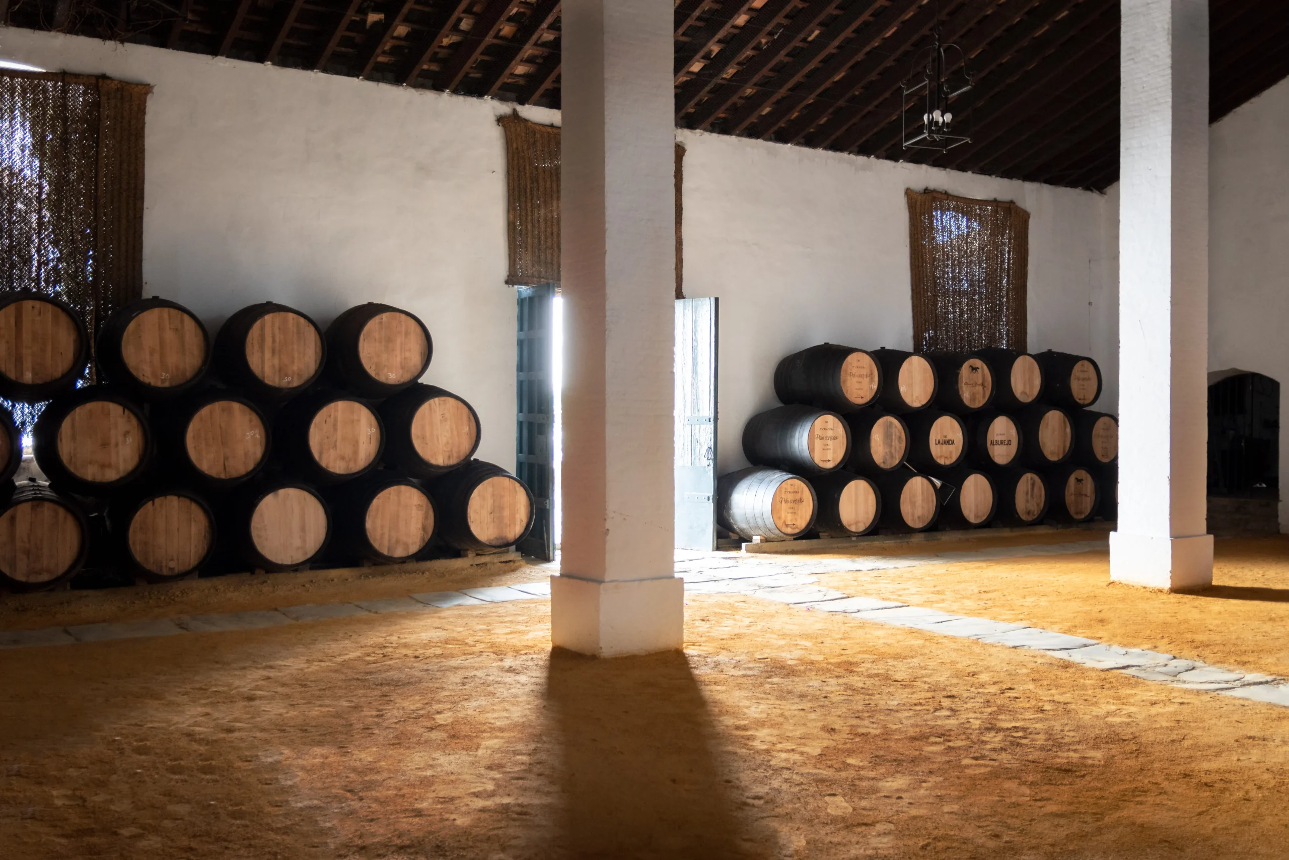 Interior de una bodega tradicional de Jerez con suelo de albero y botas de madera apiladas en andanas. Esta imagen se utiliza para ilustrar una entrada sobre por qué los vinos de Jerez no llevan añada.